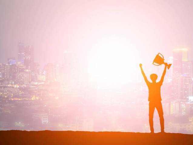 Silhouette man holding up a gold trophy cup as a winner in a competition