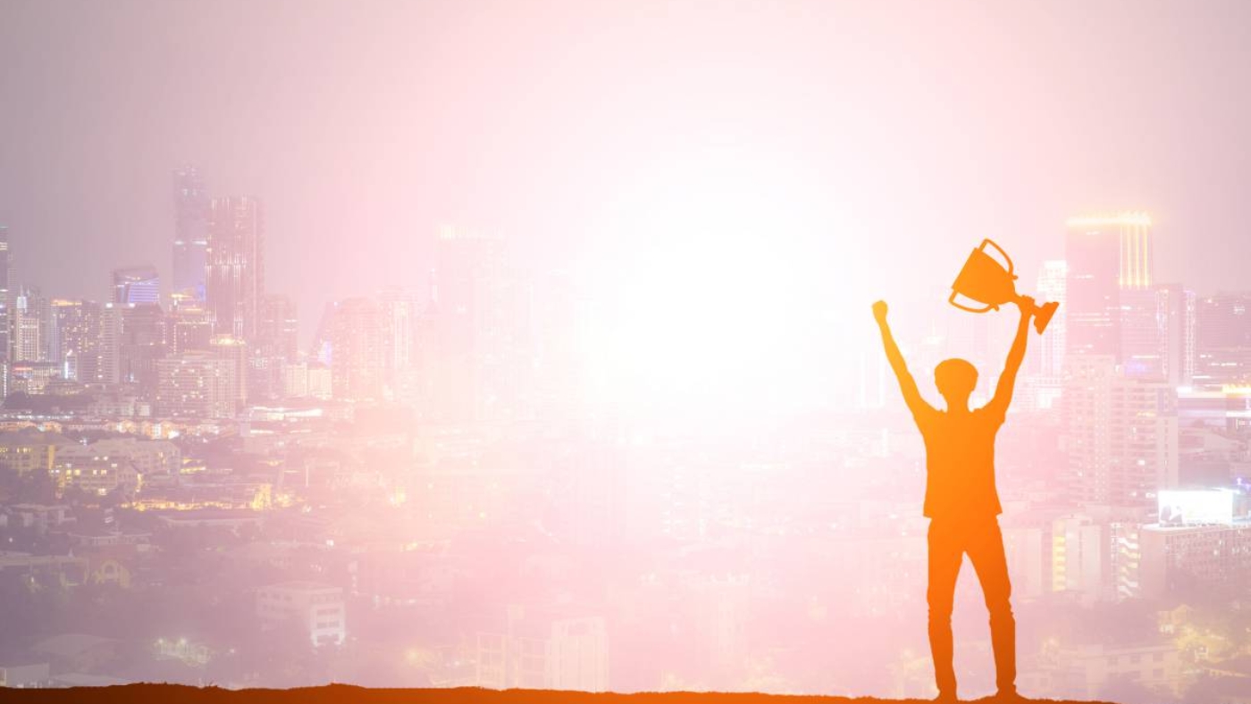 Silhouette man holding up a gold trophy cup as a winner in a competition