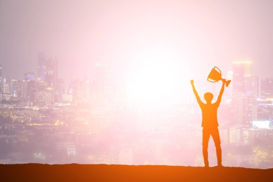 Silhouette man holding up a gold trophy cup as a winner in a competition